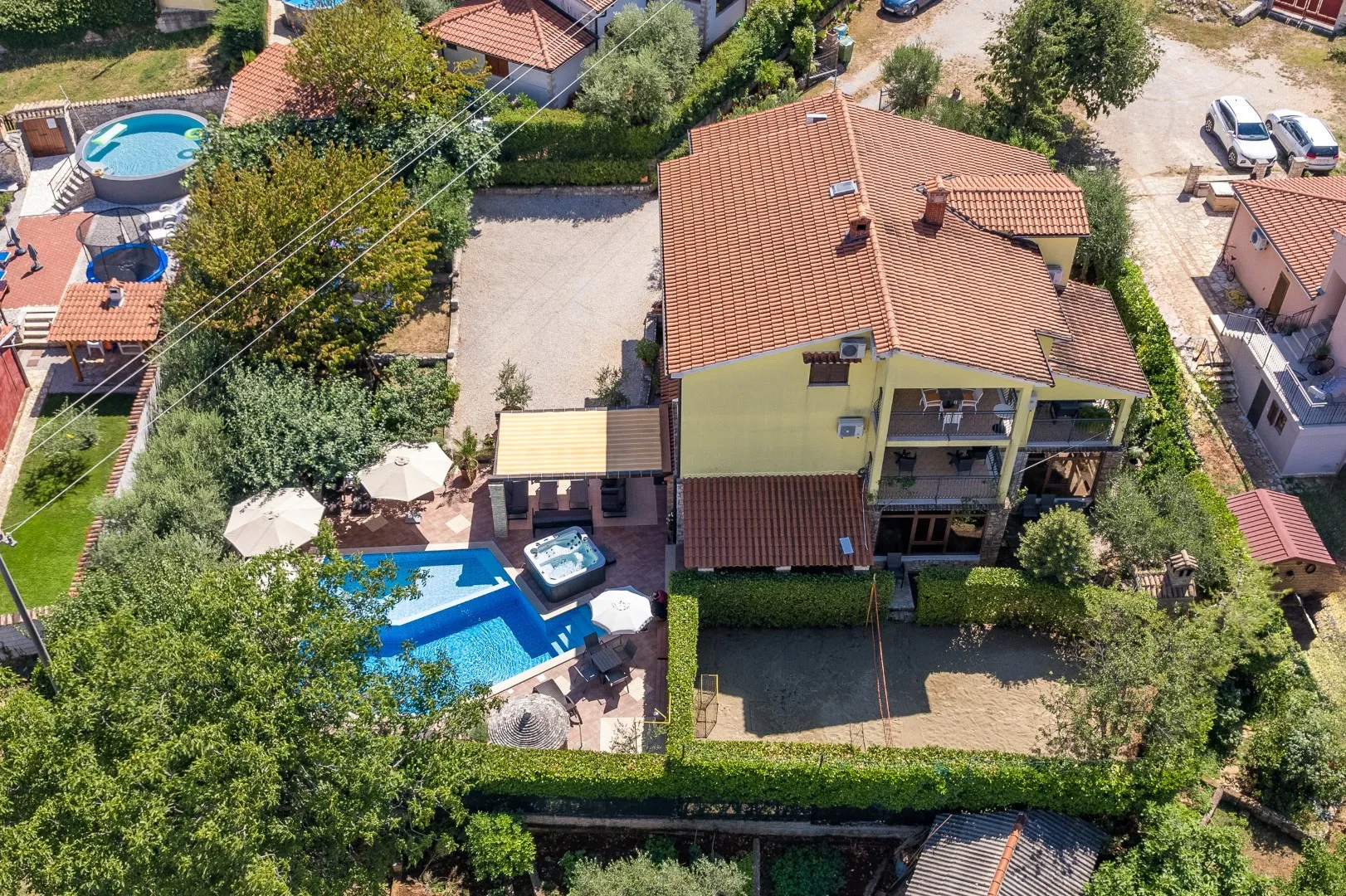 The villa from above — terracotta roof, the pool and hot tub on the terrace, and the hedged sand court alongside
