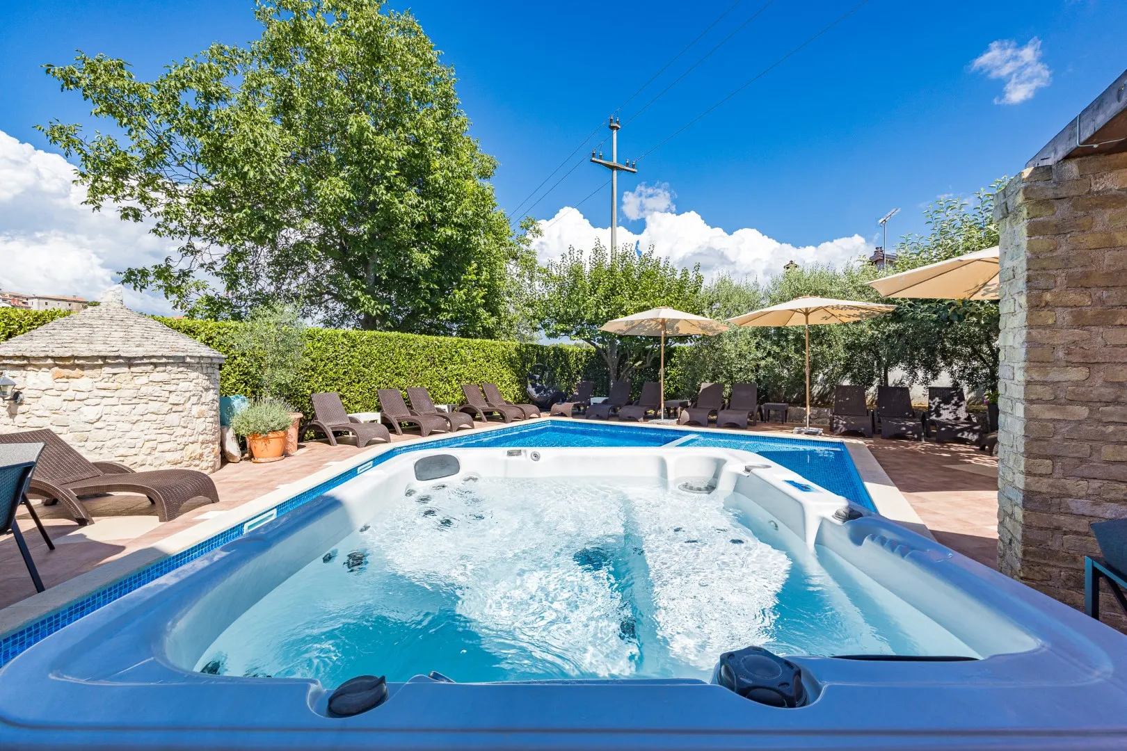 The hot tub bubbling beside the pool, with sun loungers and parasols along the far edge