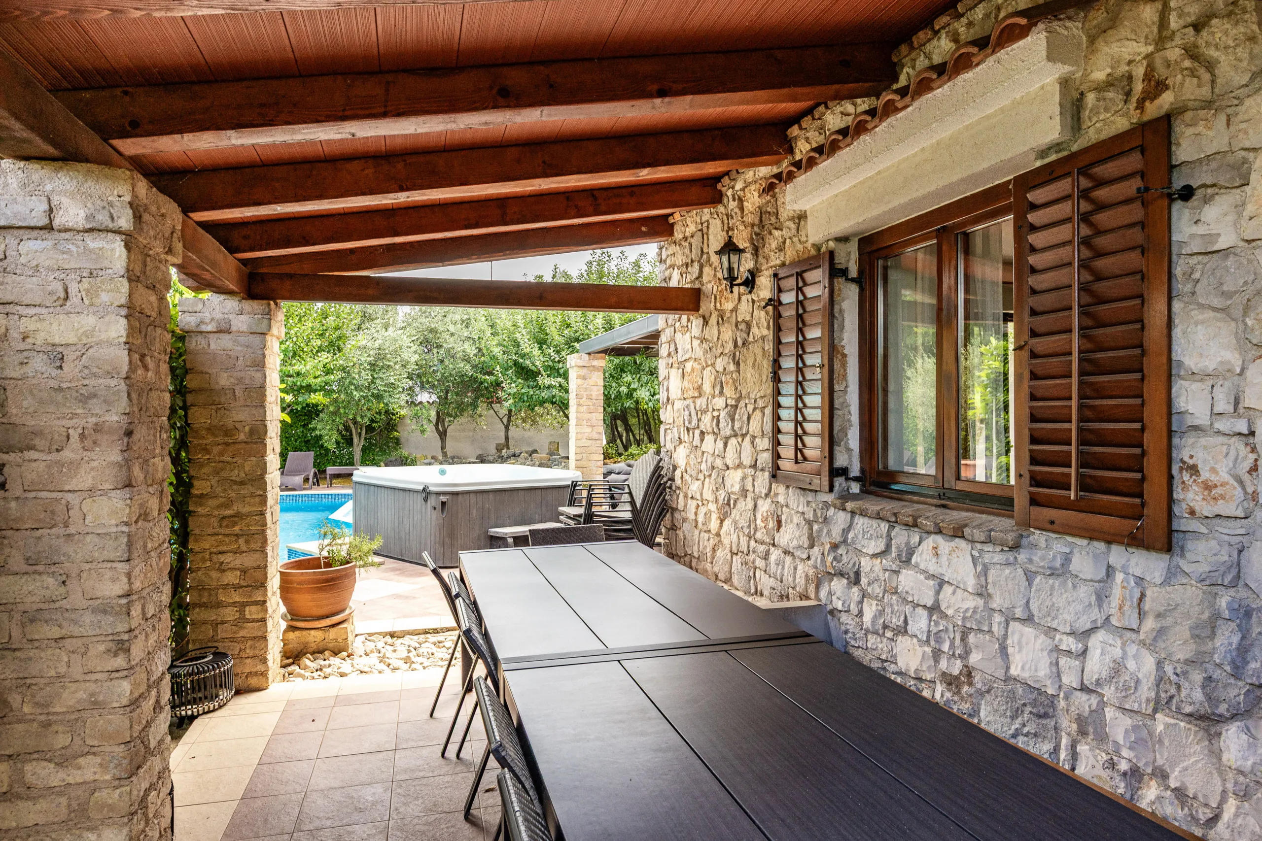 The long table under the covered stone terrace, with the hot tub and pool just beyond it