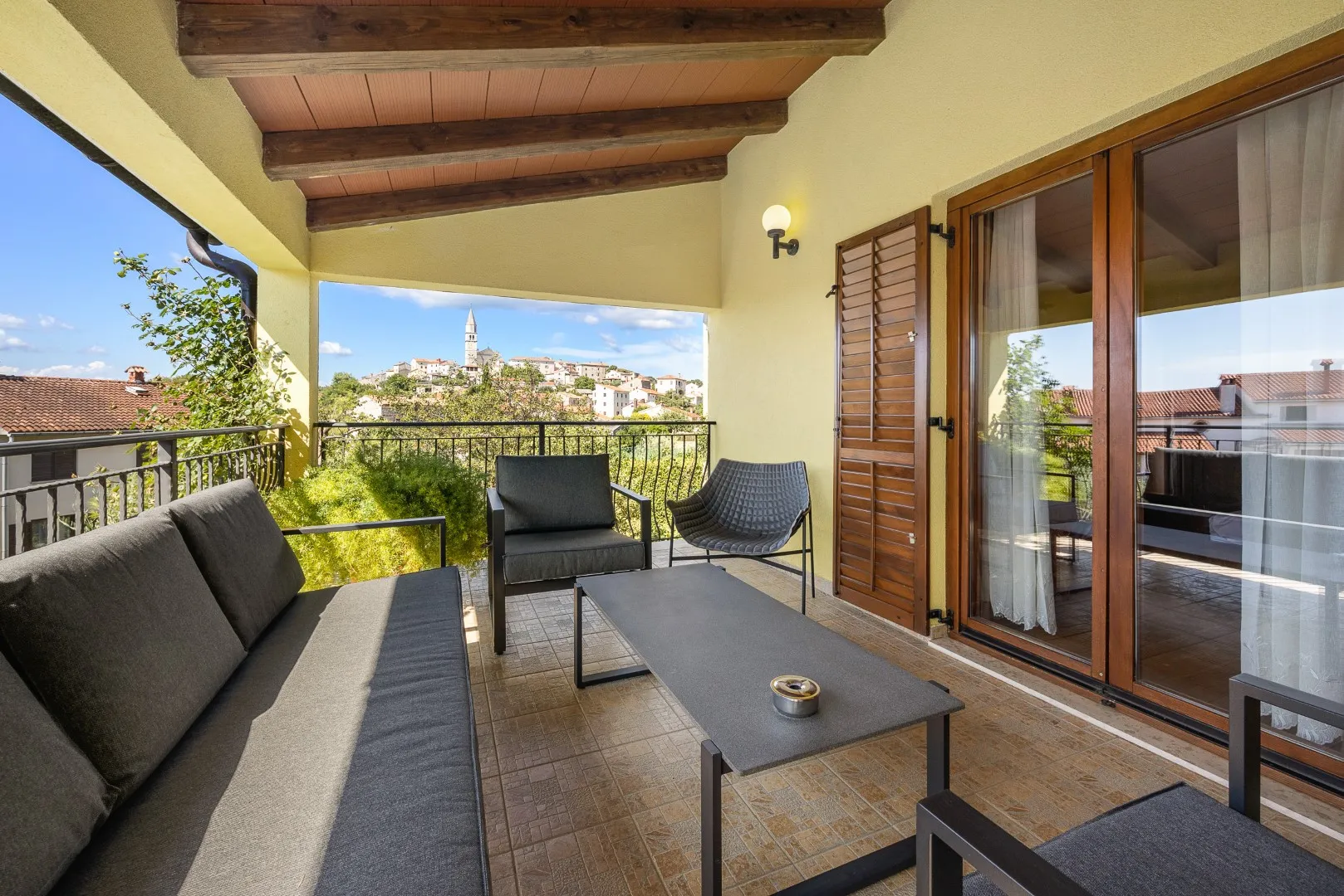 A covered balcony with lounge seating, the bell tower on the ridge opposite
