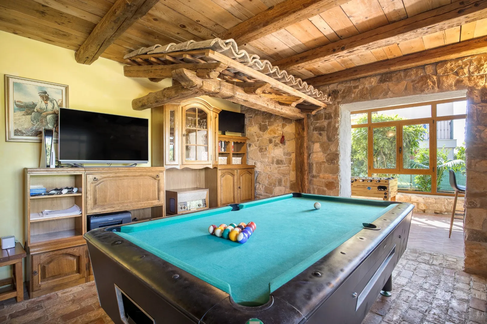 The games room: a billiards table under a beamed ceiling, bare stone walls, and table football by the window