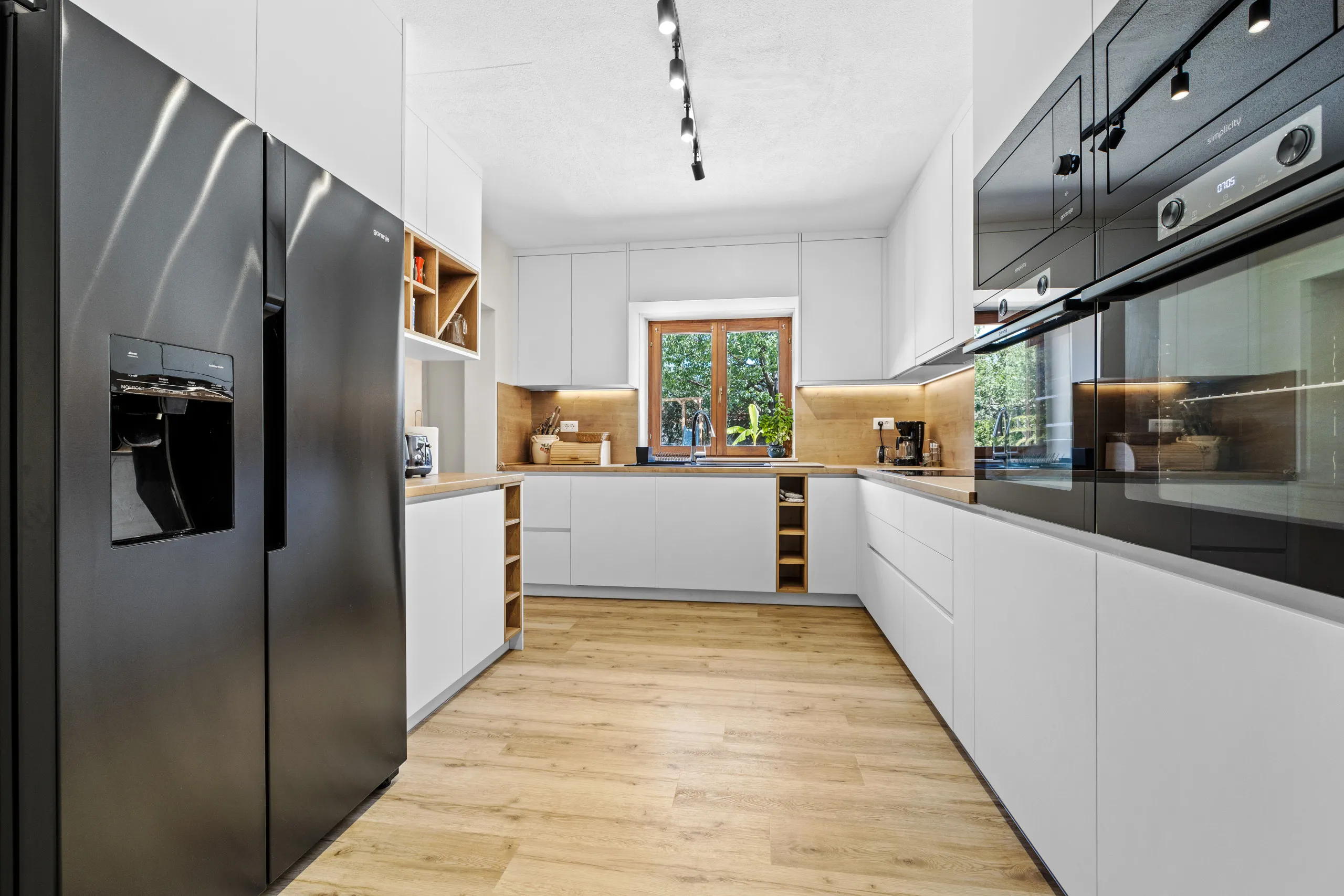 The white U-shaped kitchen with a wood worktop, built-in ovens and a tall fridge-freezer