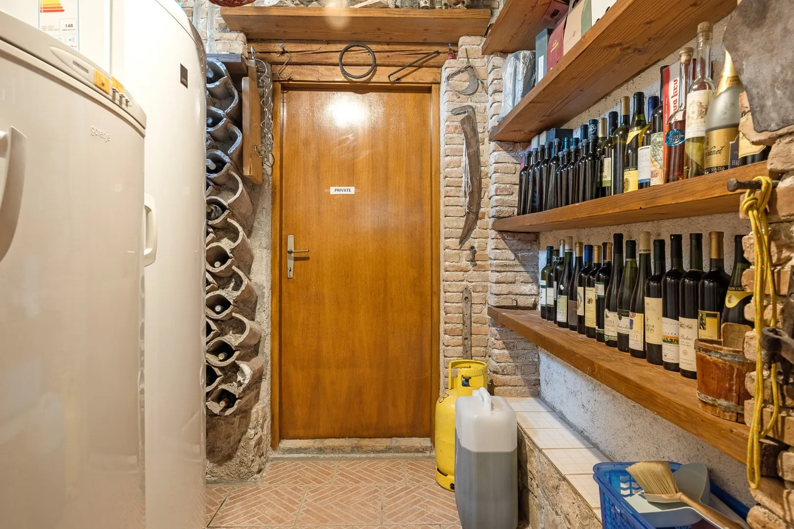 The cellar passage, wine bottles ranged along timber shelves and a stone wall