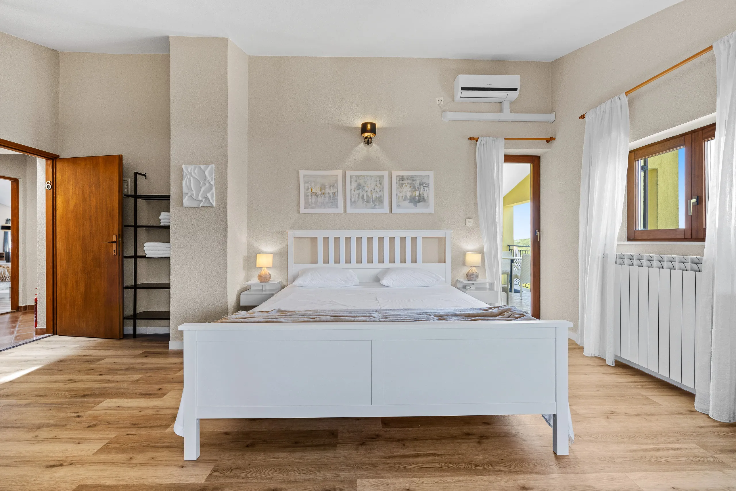 A white double bedroom with a wood floor, air conditioning and doors out to the balcony
