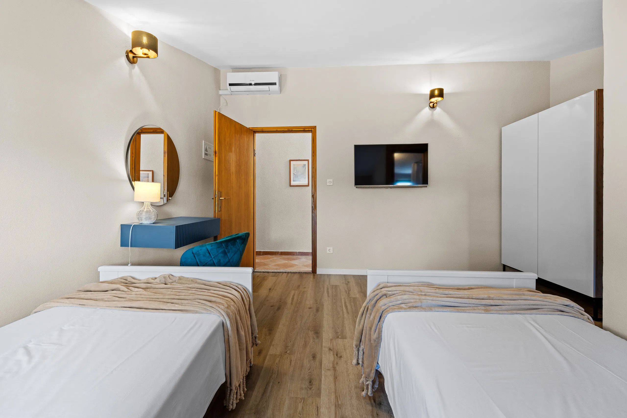 Two single beds facing a wall-mounted television and a blue dressing shelf