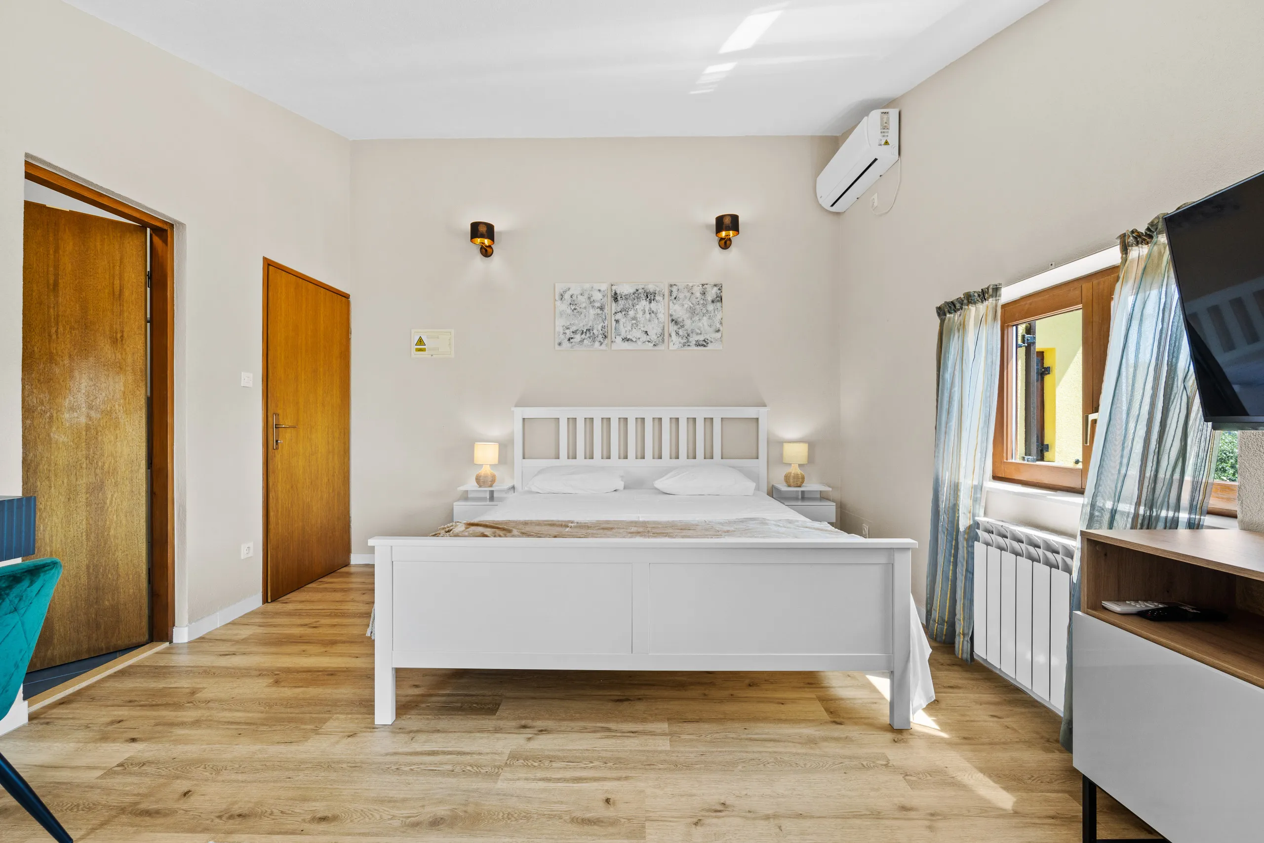 A double bedroom with wall lights, framed prints above the bed and a window onto the garden