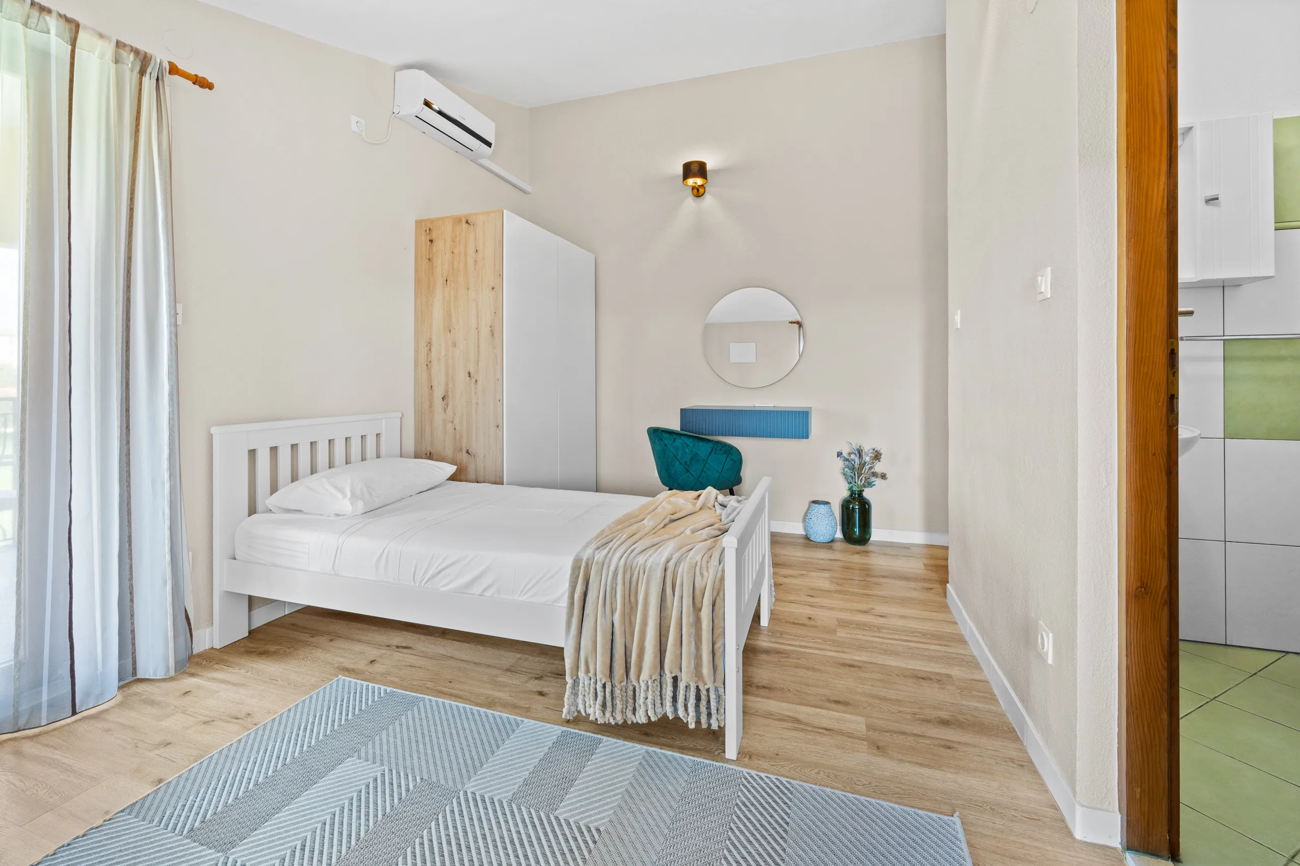 A single bedroom with a pale oak wardrobe, opening onto a small kitchen