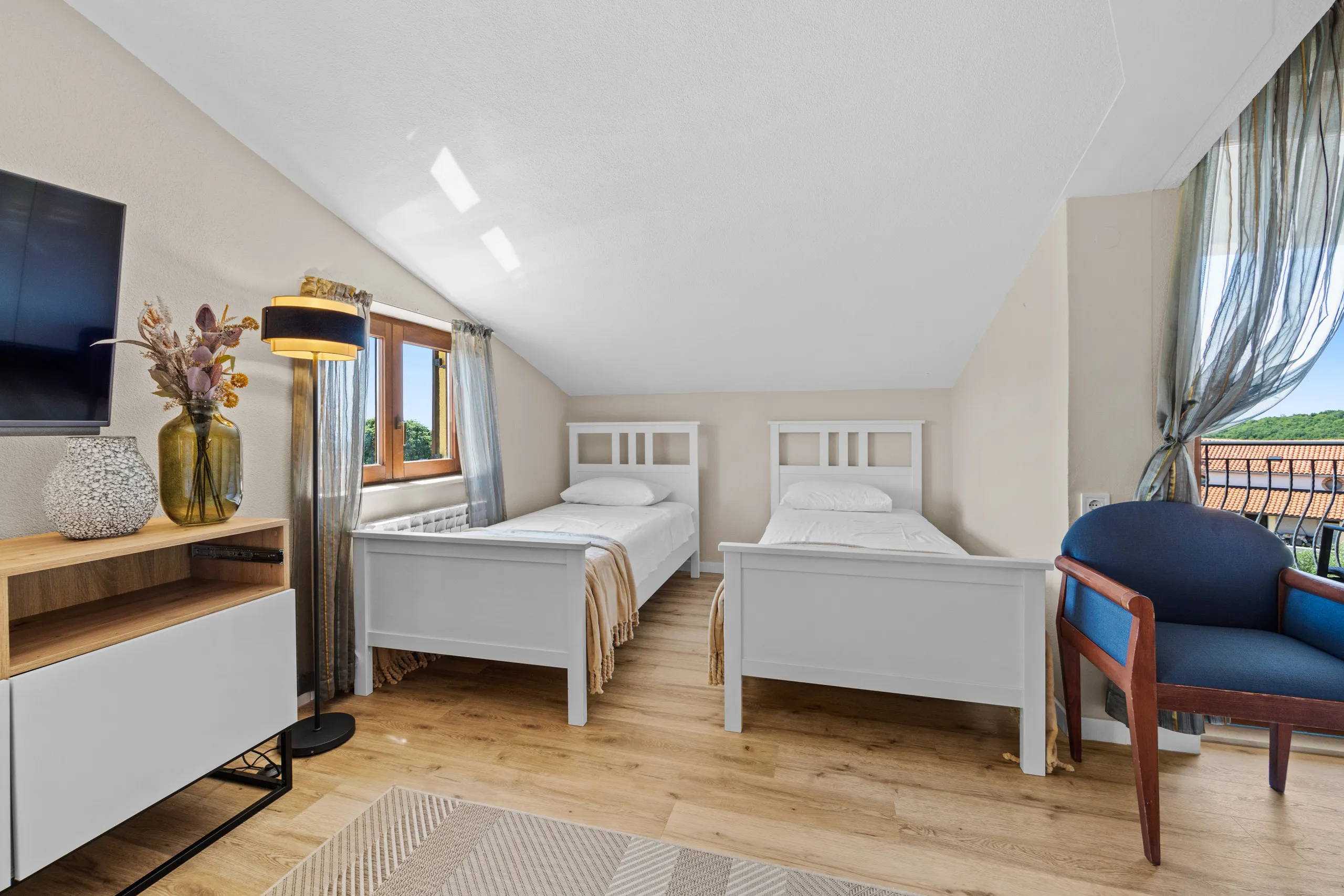 Two single beds under the eaves, a balcony door open onto the village rooftops