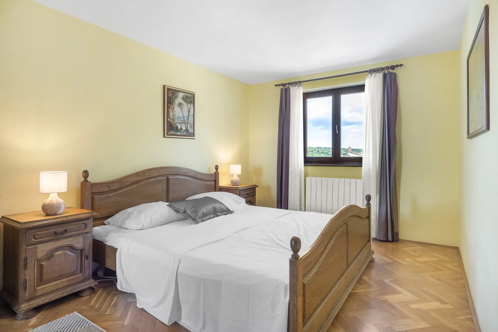 A double bedroom with pale yellow walls, a carved oak bed and a parquet floor
