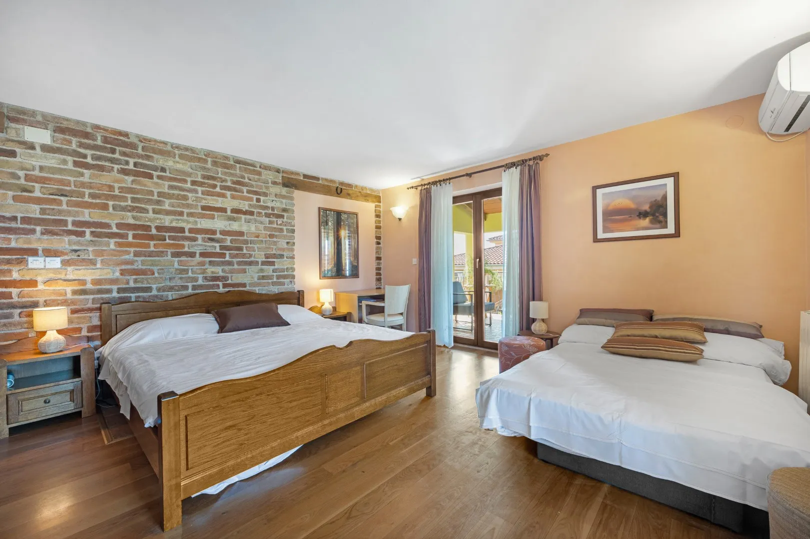 A double and a second bed in a room with an exposed brick wall and doors onto the terrace
