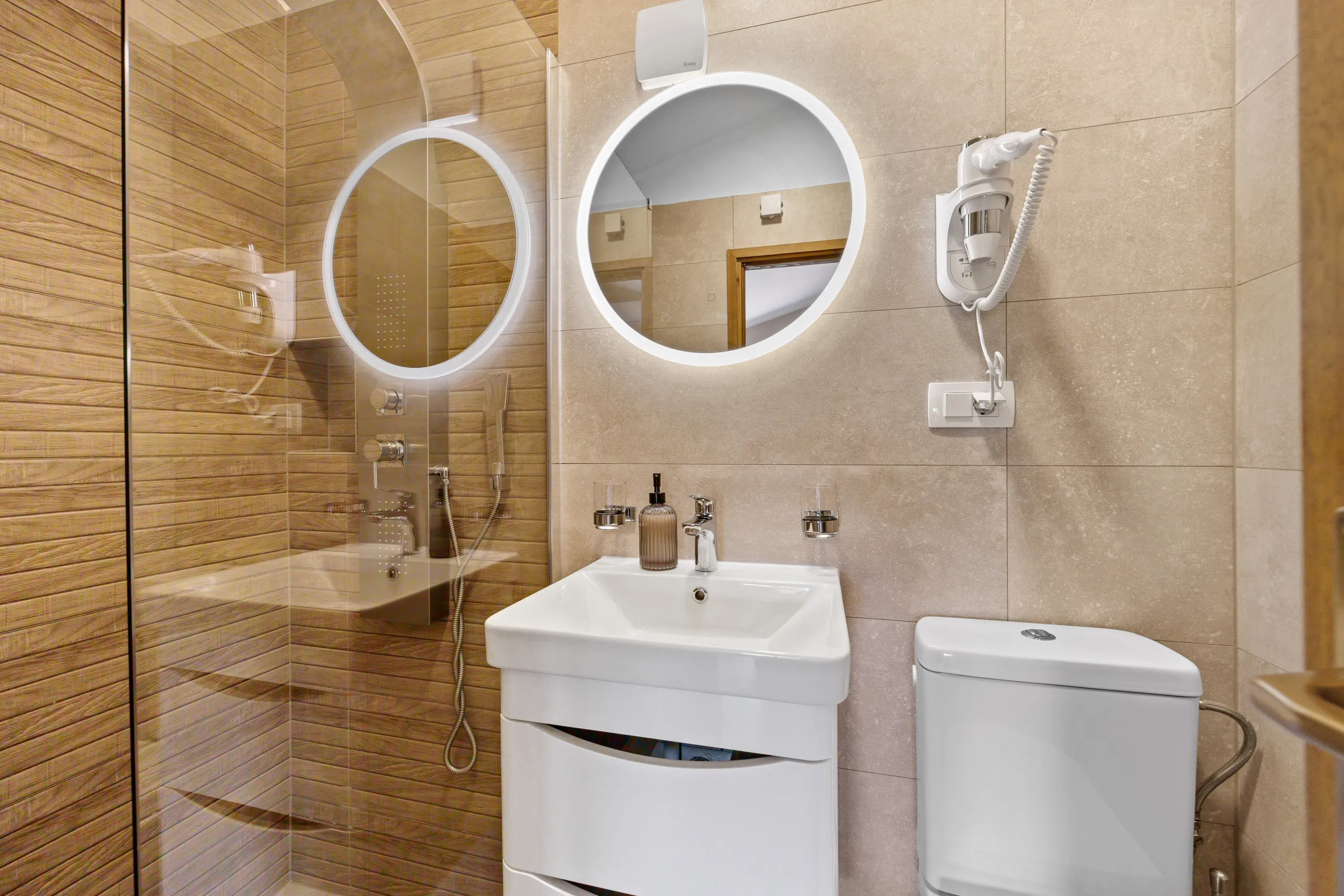 A shower room with oak-effect tiling, a round backlit mirror and a glass screen