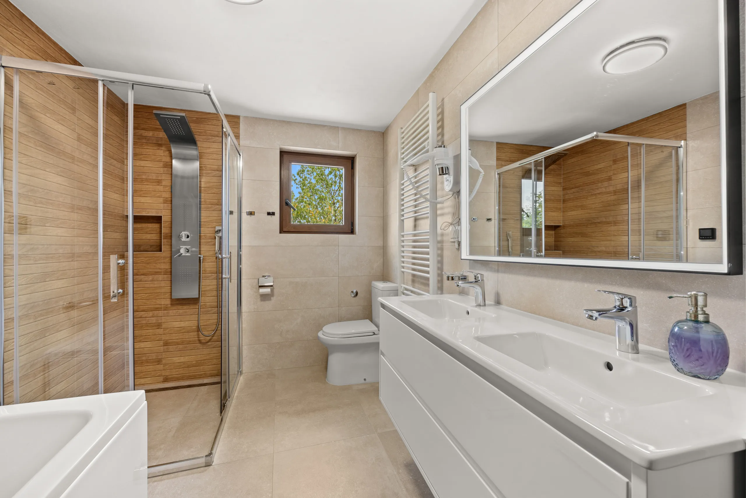 The largest bathroom — a double vanity, a corner shower, a bath and a window over the trees