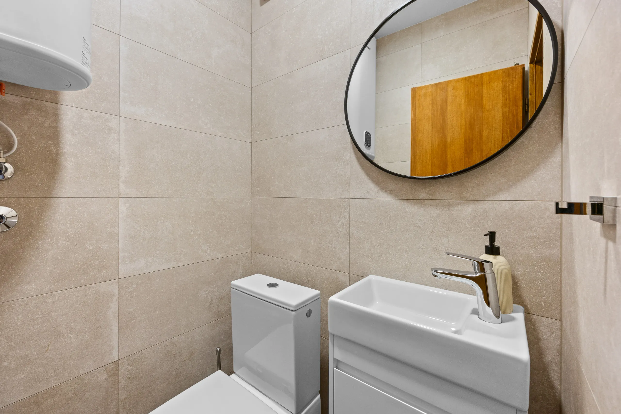 A compact WC with a round black-framed mirror above the basin